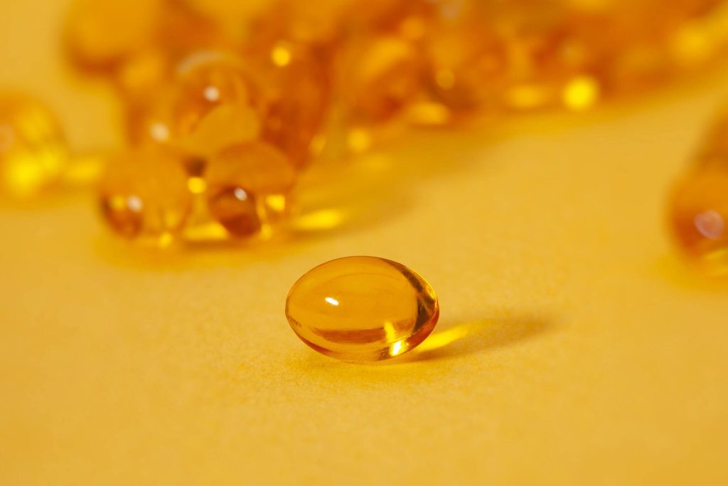 Vitamin D Gelkapseln auf gelbem Untergrund mit einer einzelnen Kapsel im Vordergrund